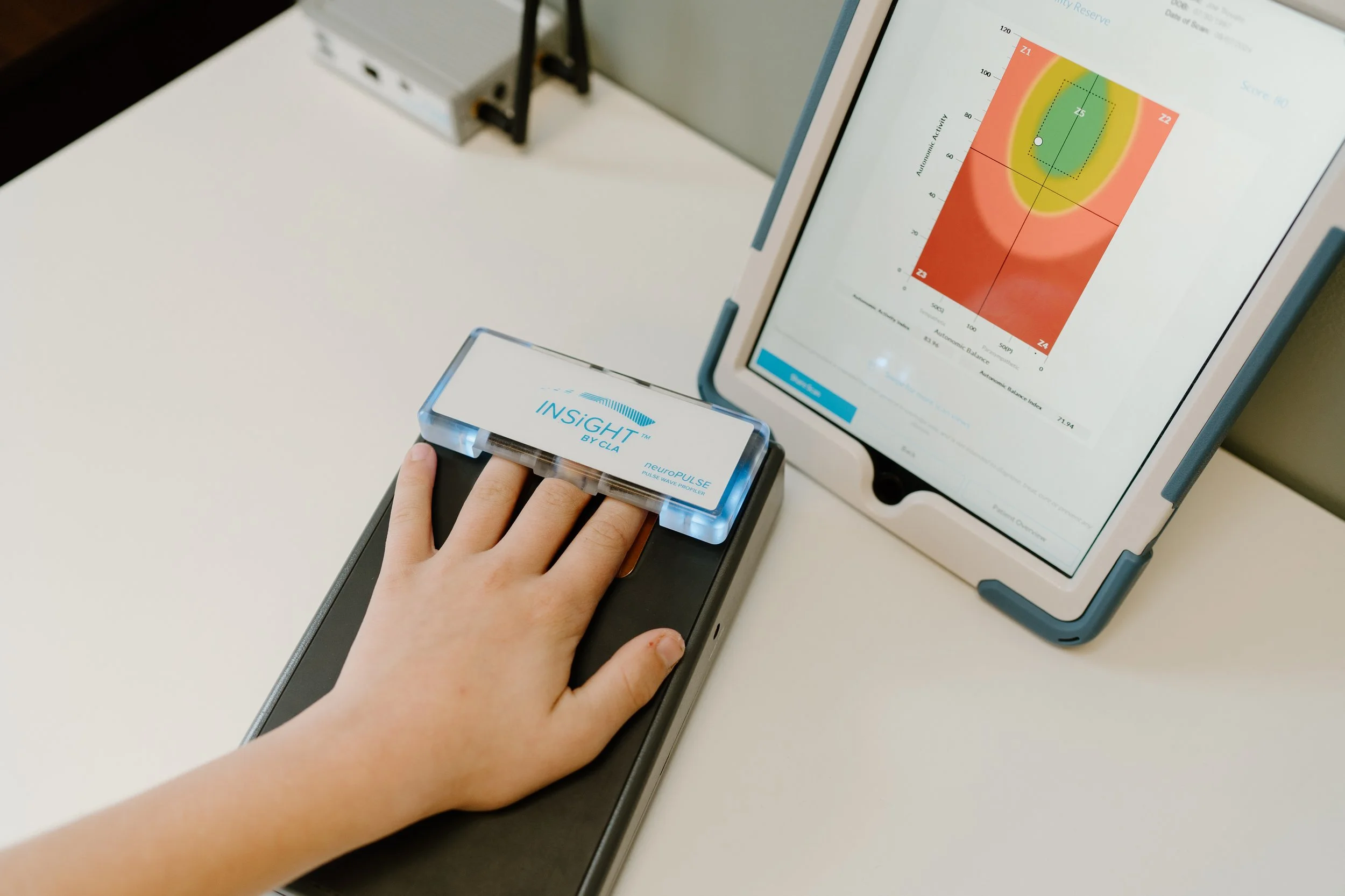 Child's hand on neuroPULSE HRV scanner with results displayed on screen